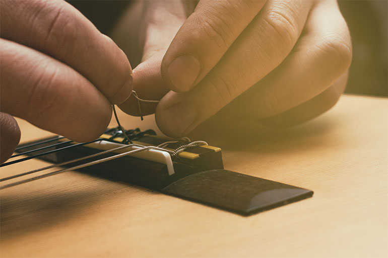close-up of hands changing strings on an acoustic guitar